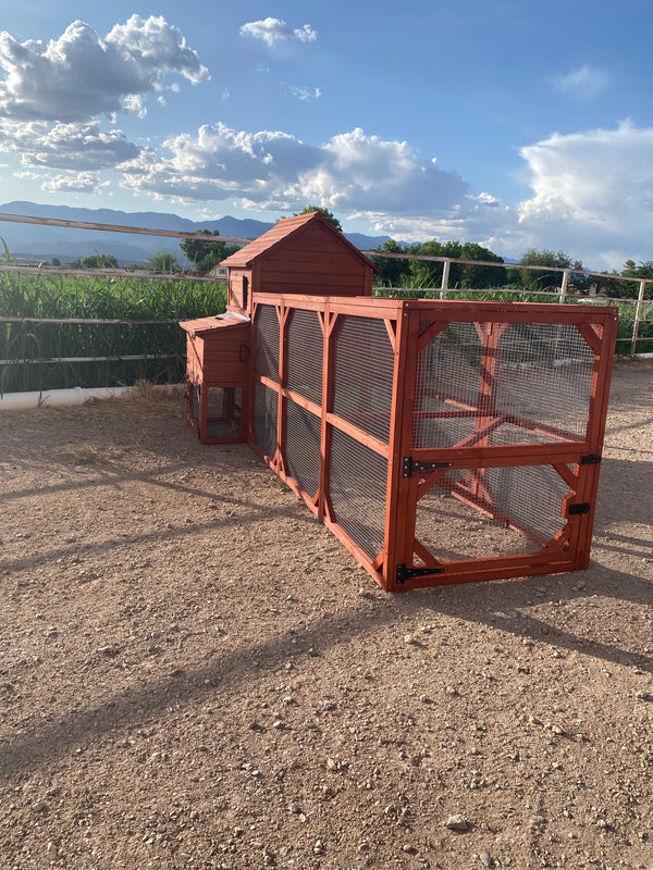 A red wooden chicken coop with a run for 6+ chickens in a rural area with mountains in the background.