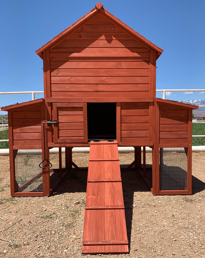 A red wooden chicken coop hen house with a central entrance ramp and wire mesh sides.